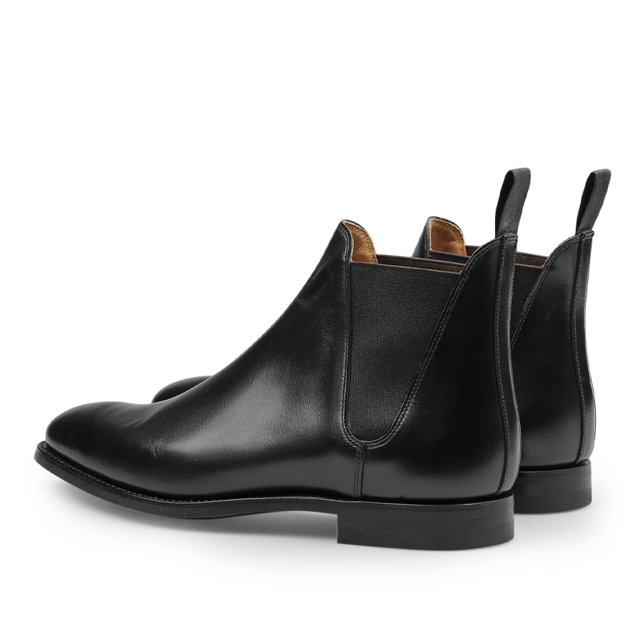 The Black Calf Leather Chelsea VIII Boots by Crockett & Jones are expertly designed with fine calf leather, pull tabs, and elastic side panels. They are elegantly displayed at an angle showcasing the Goodyear welted sole.