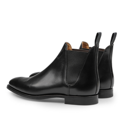 The Black Calf Leather Chelsea VIII Boots by Crockett & Jones are expertly designed with fine calf leather, pull tabs, and elastic side panels. They are elegantly displayed at an angle showcasing the Goodyear welted sole.