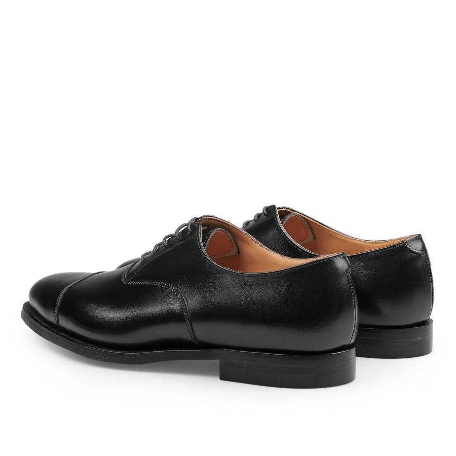 The Black Calf Leather Connaught II Cap Oxfords by Crockett & Jones, crafted from fine calf leather, are stylish dress shoes featuring a lace-up closure and durable city rubber sole, pictured from the back and side.