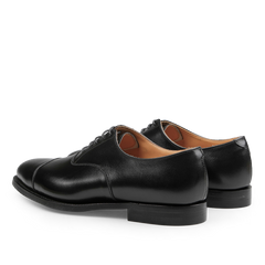 The Black Calf Leather Connaught II Cap Oxfords by Crockett & Jones, crafted from fine calf leather, are stylish dress shoes featuring a lace-up closure and durable city rubber sole, pictured from the back and side.