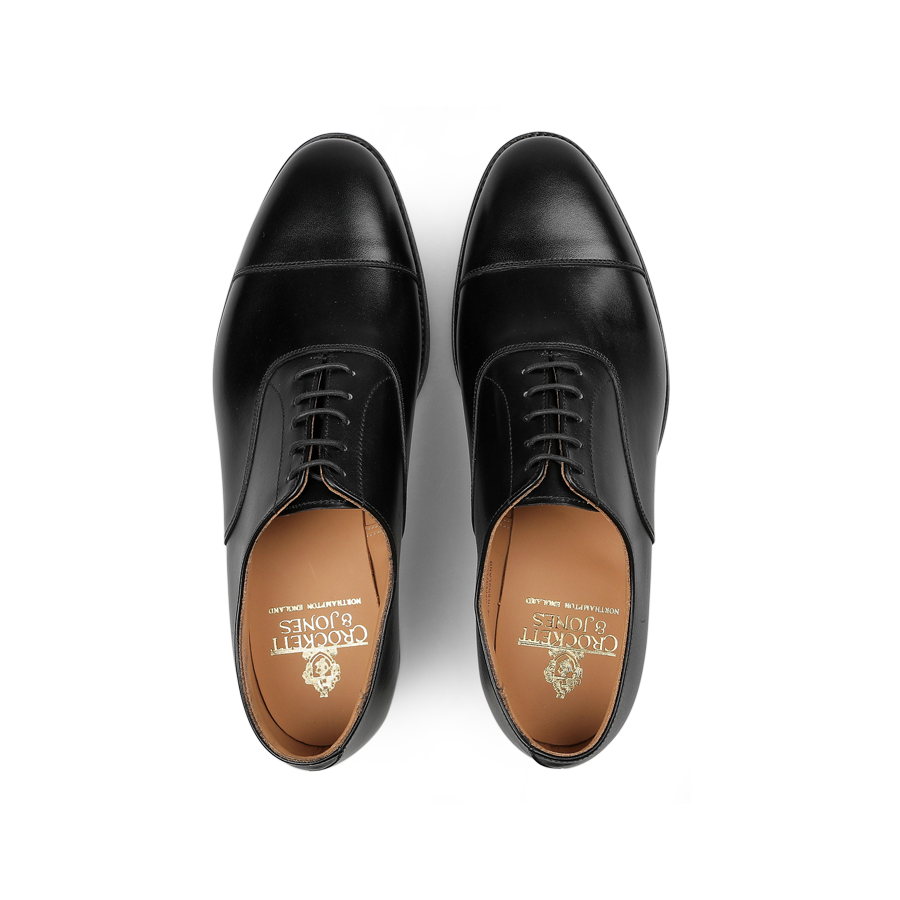 Top view of a pair of Black Calf Leather Connaught II Cap Oxfords by Crockett & Jones, featuring fine calf leather with tan insoles and a city rubber sole.