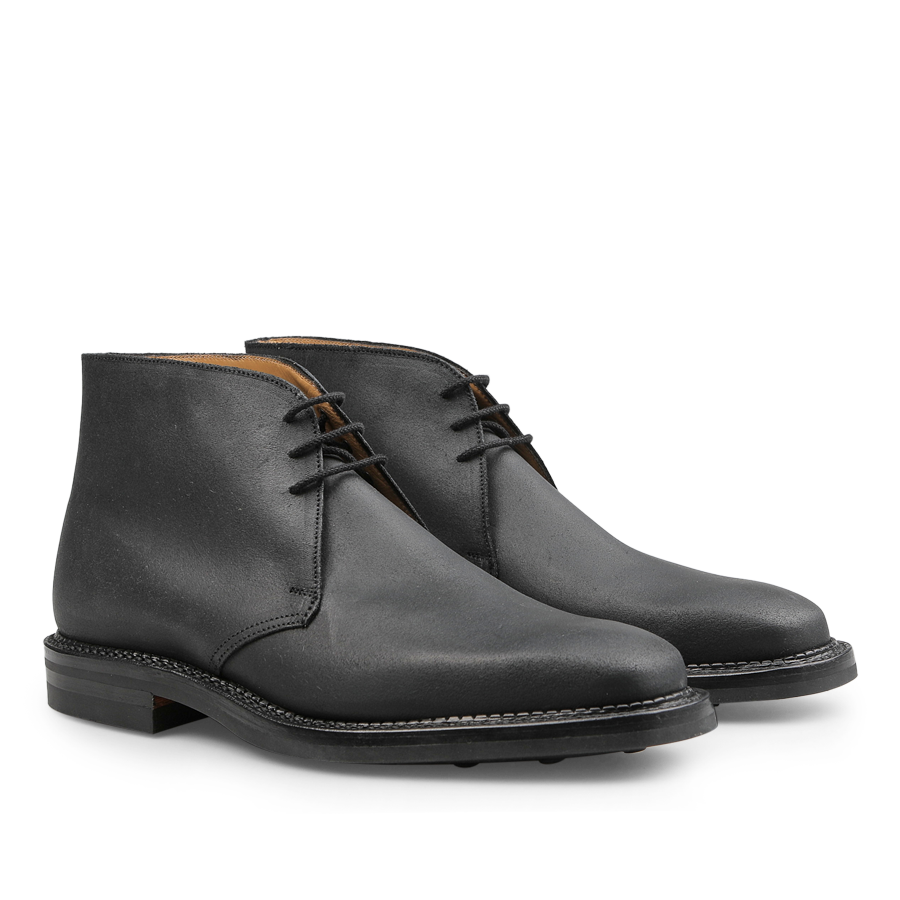 A pair of Black Rough-Out Suede Molton Boots by Crockett & Jones, featuring Goodyear welted craftsmanship with black laces and brown soles, showcased against a pristine white background.