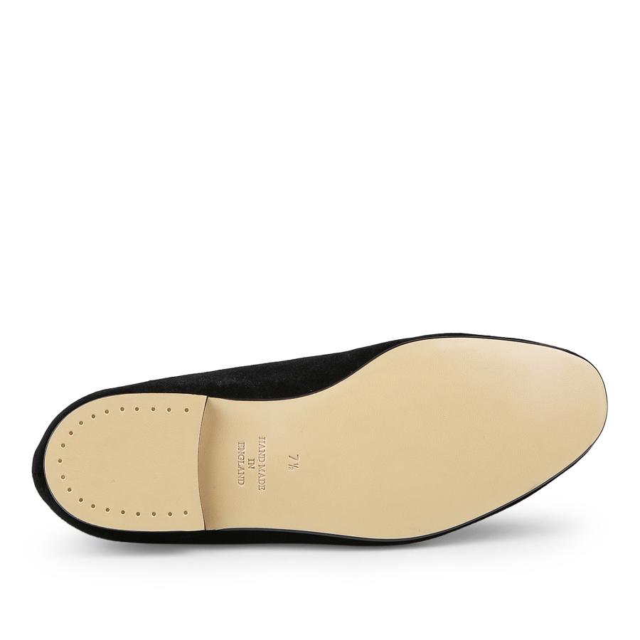 The Black Velvet Lion Rampant Albert Slippers by Crockett & Jones feature a tan sole with small perforations near the heel, visible from the bottom of the single black shoe, crafted from durable leather for longevity.