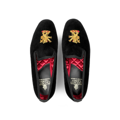 A pair of Black Velvet Lion Rampant Albert Slippers by Crockett & Jones, featuring hand-embroidered gold crests, a red quilted interior lining, and durable leather soles.