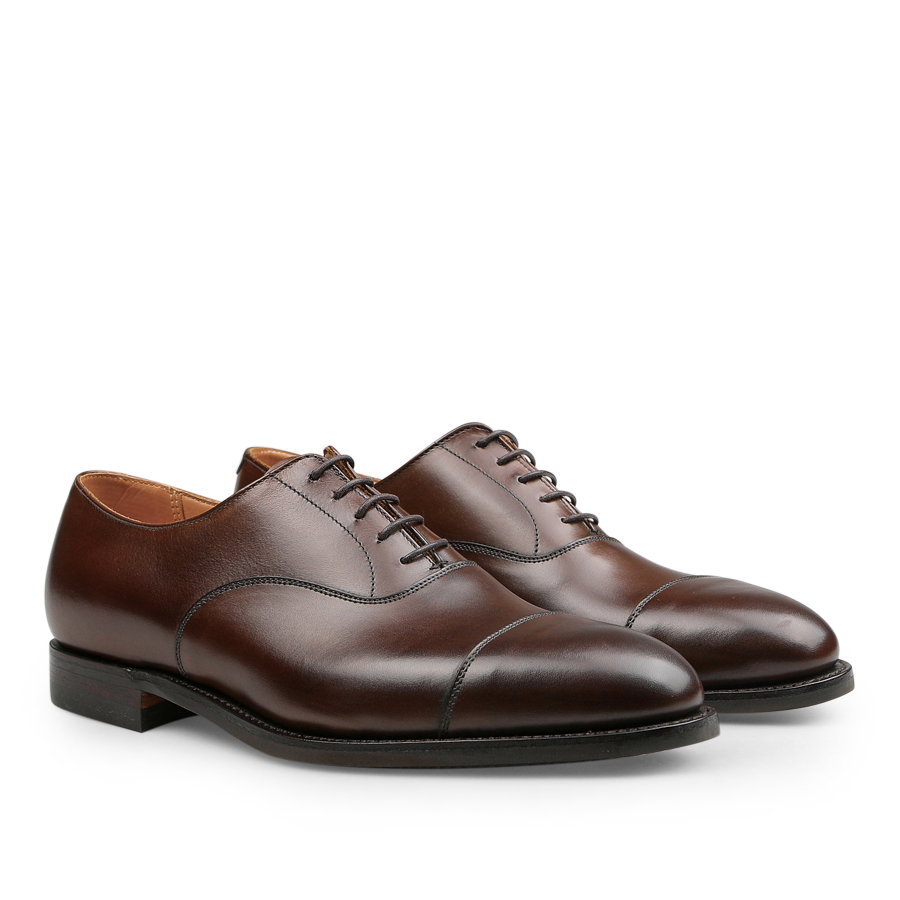 A pair of Crockett & Jones Dark Brown Burnished Calf Connaught Cap Oxfords, which boast an elegant design with a stylish cap toe crafted from dark brown burnished calf leather and durable black Goodyear-welted soles.