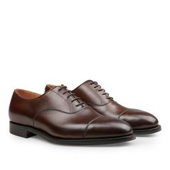 A pair of Crockett & Jones Dark Brown Burnished Calf Connaught Cap Oxfords, which boast an elegant design with a stylish cap toe crafted from dark brown burnished calf leather and durable black Goodyear-welted soles.