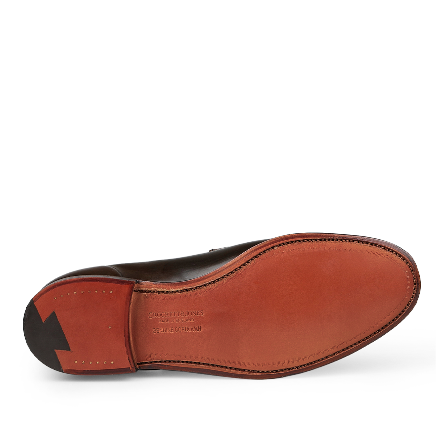 The image displays the sole of a pair of Crockett & Jones Dark Brown Cordovan Leather Harvard Loafers, showcasing a Goodyear-welted design with a stitched border and a textured black rubber heel.