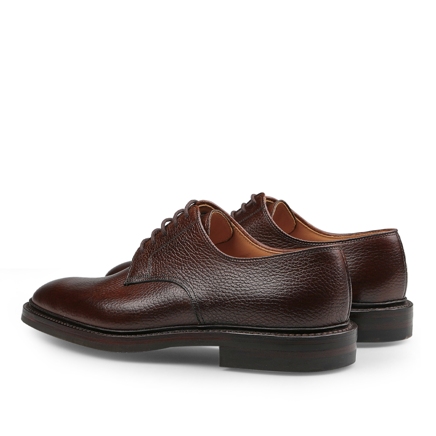 The Dark Brown Country Calf Grain Ashdown Derbies from Crockett & Jones, made with Goodyear-welted construction and laces, showcase a textured finish. Displayed on a white backdrop, these shoes exude an elegant and timeless style when viewed from the back and side.