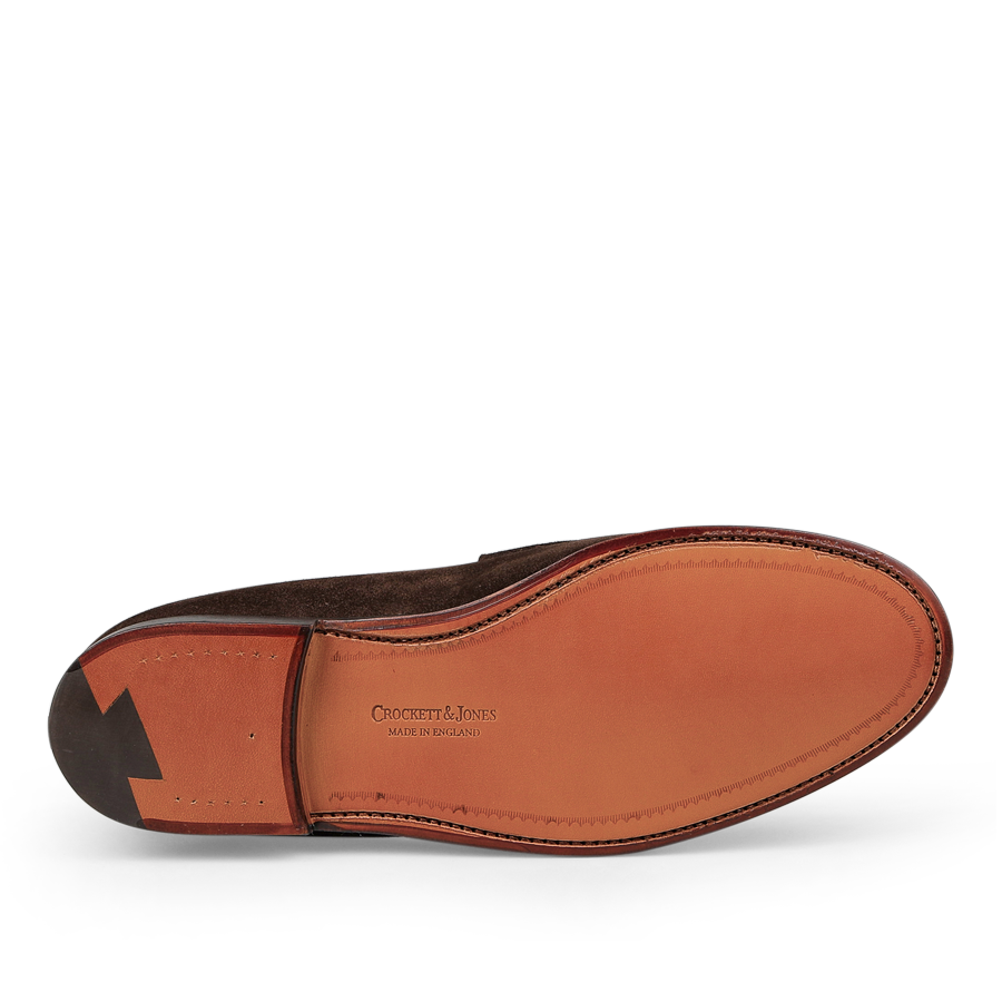 The Dark Brown Suede Leather Boston Loafers from Crockett & Jones boast a timeless penny loafer design, complete with a Goodyear-welted brown leather sole that is tastefully embossed with "Crockett & Jones" and "Made in England" at the center.