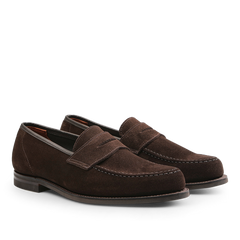 Positioned side by side on a plain background is a pair of Crockett & Jones Dark Brown Suede Leather Harvard II Loafers, showcasing their stitching details and low heels.