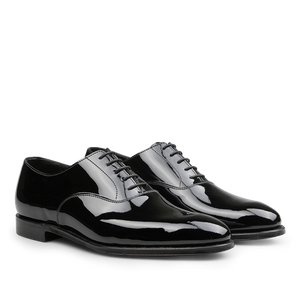 The Black Patent Calf Leather Overton Oxfords by Crockett & Jones are beautifully crafted, featuring a sleek black patent calf leather design that elegantly shines against a white background, finished with meticulously tied black laces.