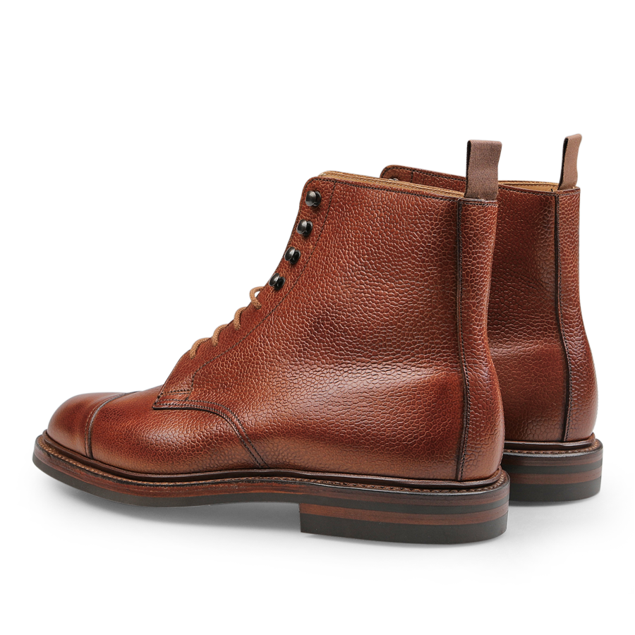 Tan Scotch Grain Leather Coniston Boots by Crockett & Jones feature brown leather with black laces and stitching detail. These boots are crafted from Scotch grain leather, equipped with pull tabs at the back and flat soles, perfectly combining rugged style with an elegant twist reflecting a classic Crockett & Jones design.