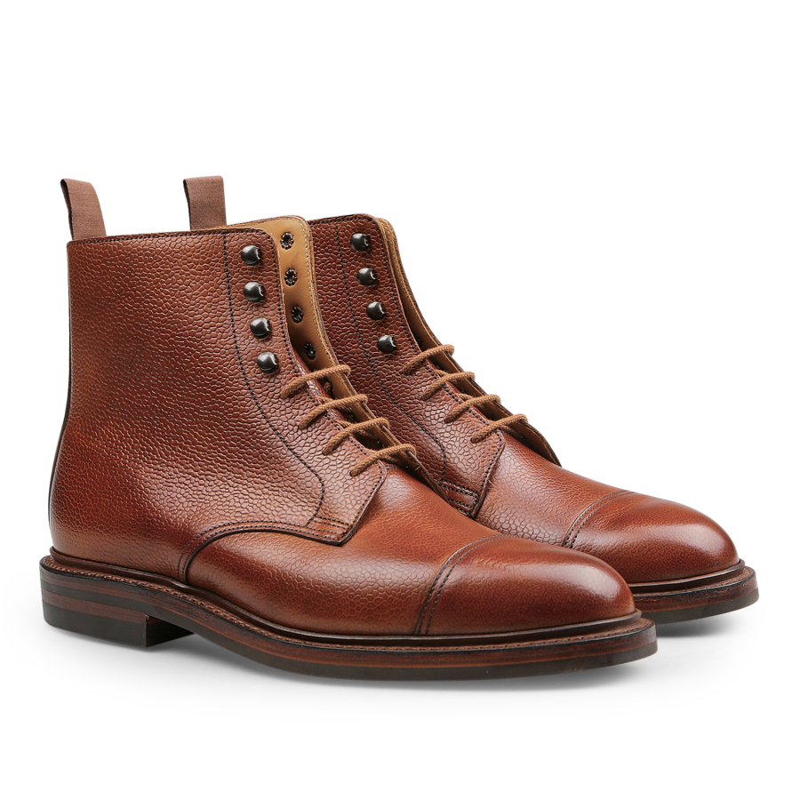 A pair of Tan Scotch Grain Leather Coniston Boots by Crockett & Jones, showcasing a textured finish, cap toe design, metal eyelets, and pull tabs at the back, reminiscent of the classic derby boot style.