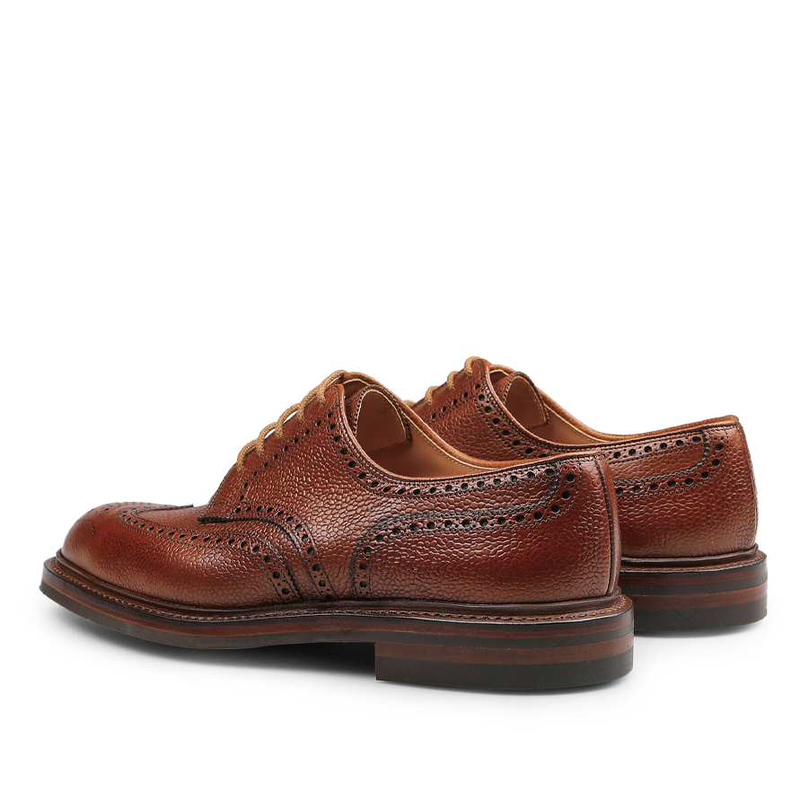 Tan Pembroke brogues by Crockett & Jones, made from luxurious Scotch grain leather, highlight intricate perforations and durable Goodyear-welted soles, shown from a rear and angled perspective.