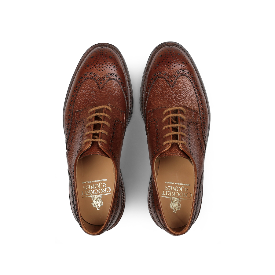 A pair of Tan Scotch Grain Leather Pembroke Brogues from Crockett & Jones, crafted with laces and featuring decorative perforations, a visible shoe label, and classic Goodyear-welted construction.