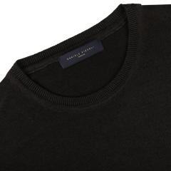 Close-up of a dark brown crew neck sweater, crafted from luxurious merino wool, with a dark label sewn inside the collar displaying "Daniele Fiesoli" in gold lettering.