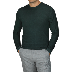 Person wearing a Dark Green Merino Wool Crewneck by Daniele Fiesoli and gray trousers, with hands in pockets, against a plain, light background.