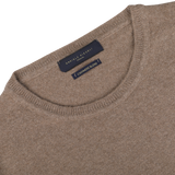 A close-up of the neckline of a light brown wool-cashmere crewneck sweater with a dark blue label that reads "Daniele Fiesoli Fine Knit.