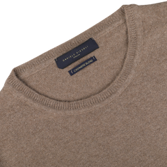 A close-up of the neckline of a light brown wool-cashmere crewneck sweater with a dark blue label that reads "Daniele Fiesoli Fine Knit.