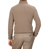 A man is seen from behind wearing a light brown quarter-zip sweater and brown pants. His right hand is in his pocket, showcasing the casual elegance of an absolutely made in Italy wool-cashmere blend garment by Daniele Fiesoli.