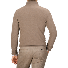 A man is seen from behind wearing a light brown quarter-zip sweater and brown pants. His right hand is in his pocket, showcasing the casual elegance of an absolutely made in Italy wool-cashmere blend garment by Daniele Fiesoli.