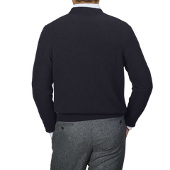 A person wearing a navy blue cashmere crewneck sweater by Daniele Fiesoli and gray pants is seen from the back against a gray background.