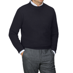 A person stands against a gray backdrop, stylishly wearing the Navy Blue Cashmere Crewneck Sweater by Daniele Fiesoli over a white collared shirt, paired with gray pants.