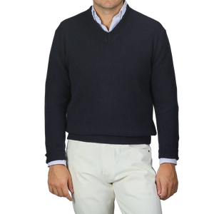 A person is stylishly dressed in a Daniele Fiesoli Navy Blue Cashmere V-Neck Sweater, crafted from upcycled cashmere, over a light blue collared shirt paired with crisp white pants.