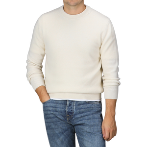 A person wearing a Nuvola Ecru Cashmere Crewneck Sweater by Daniele Fiesoli and blue jeans stands with one hand in their pocket.