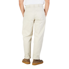 Rear view of a person wearing De Bonne Facture's undyed heavy cotton drill balloon trousers and brown suede shoes, standing against a white background.