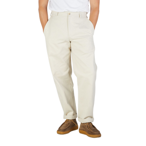 A close-up of a person wearing De Bonne Facture's Undyed Heavy Cotton Drill Balloon Trousers and brown suede shoes, standing against a plain background.