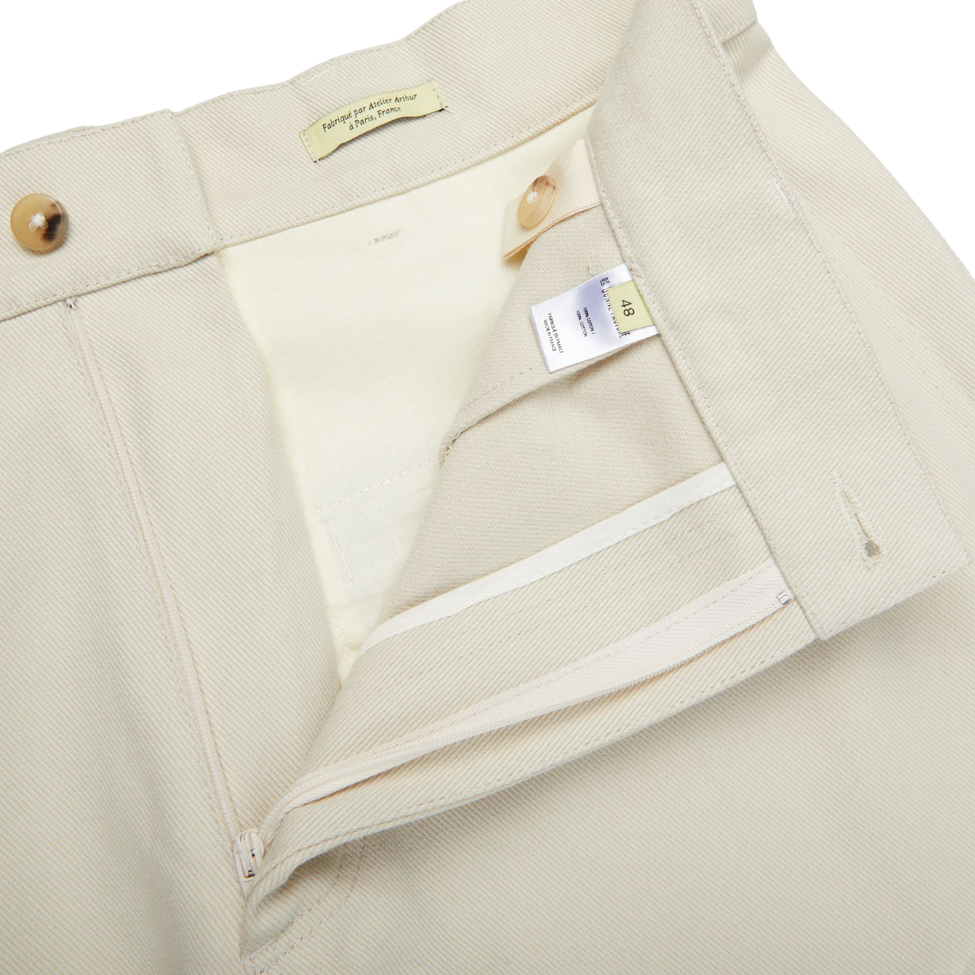 Close-up of a beige jacket collar displaying visible branding tags and a partially unzipped inner lining made of De Bonne Facture Undyed Heavy Cotton Drill Balloon Trousers.