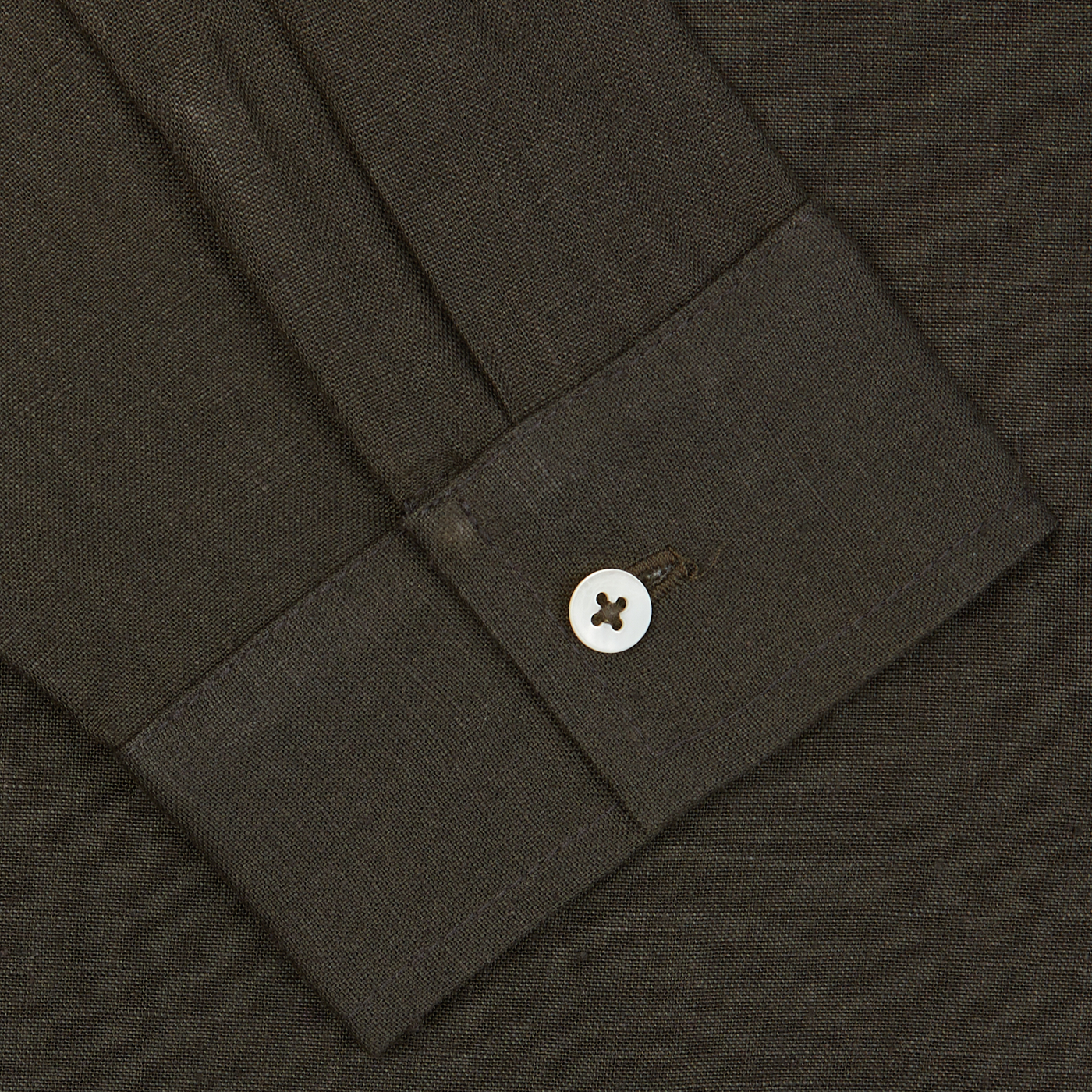 Close-up of a dark brown De Bonne Facture Arabica Green Linen Canvas Painter's Jacket sleeve with a buttoned cuff.