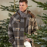 A man wearing a De Bonne Facture Brown Undyed Shepherds Check Wool Duffle Coat in front of a Christmas tree.
