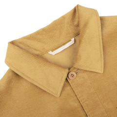 Close-up of the De Bonne Facture Gold Mustard Cotton Corduroy Work Jacket, highlighting the collar, a single button, and part of the body fabric against a plain background.