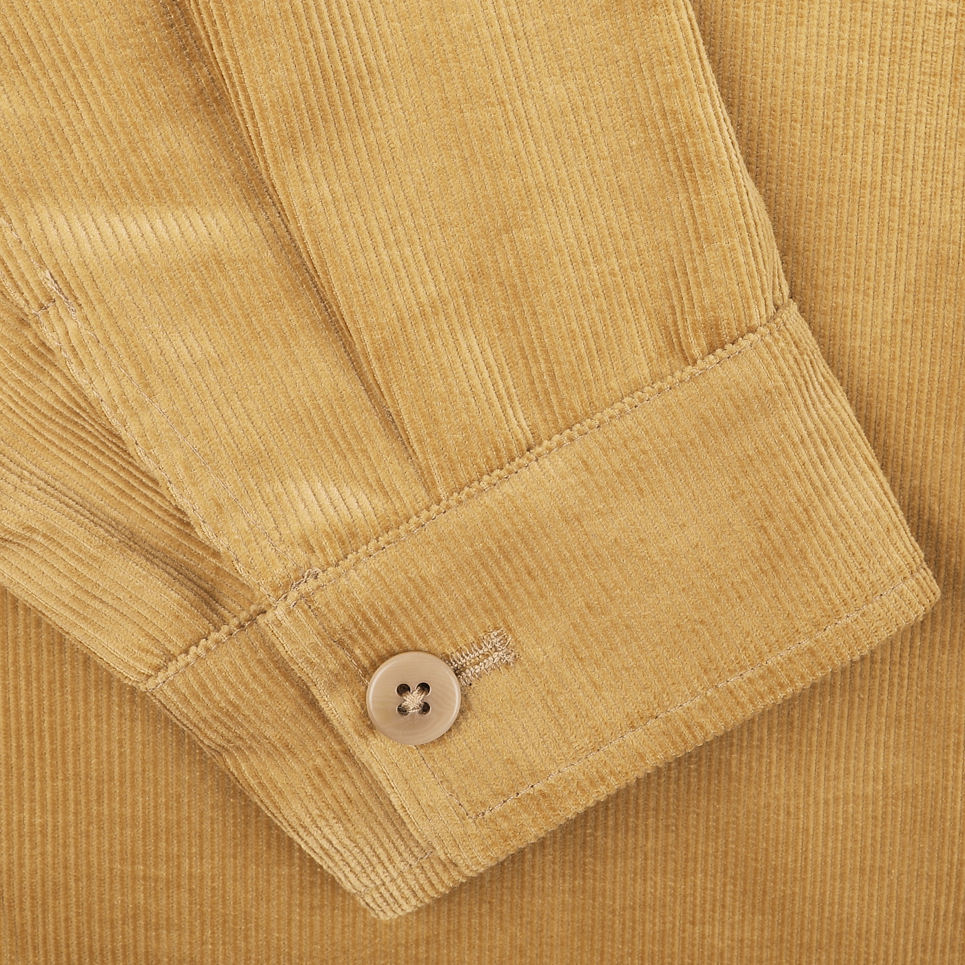 Close-up of a beige corduroy fabric sleeve with a beige button securing the cuff, reminiscent of De Bonne Facture's Gold Mustard Cotton Corduroy Work Jacket.