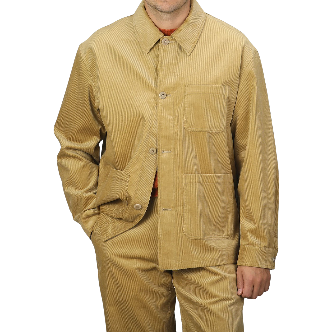 A person wearing the Gold Mustard Cotton Corduroy Work Jacket from De Bonne Facture with a collar and large front pockets, matching tan pants, and an orange shirt underneath, against a plain gray background.