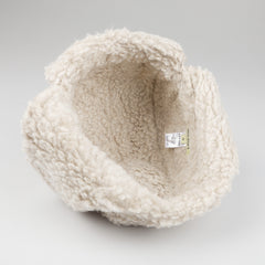 A De Bonne Facture Natural Wool Fleece Chapka Hat, featuring a fluffy cream-colored design, is open on a plain gray surface, displaying the label inside.