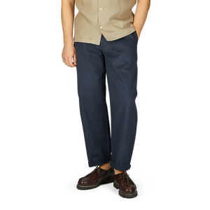 A man wearing a beige short-sleeve shirt, De Bonne Facture navy blue heavy cotton drill balloon trousers, and brown shoes on a white background.