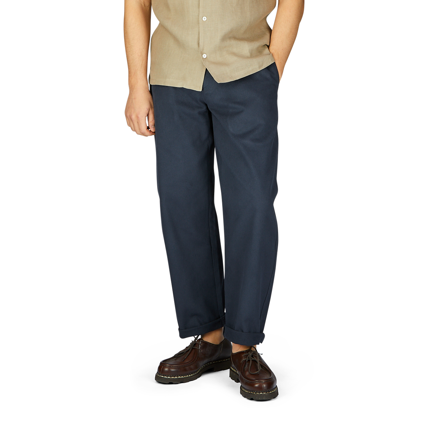 A man wearing a beige short-sleeve shirt, De Bonne Facture navy blue heavy cotton drill balloon trousers, and brown shoes on a white background.