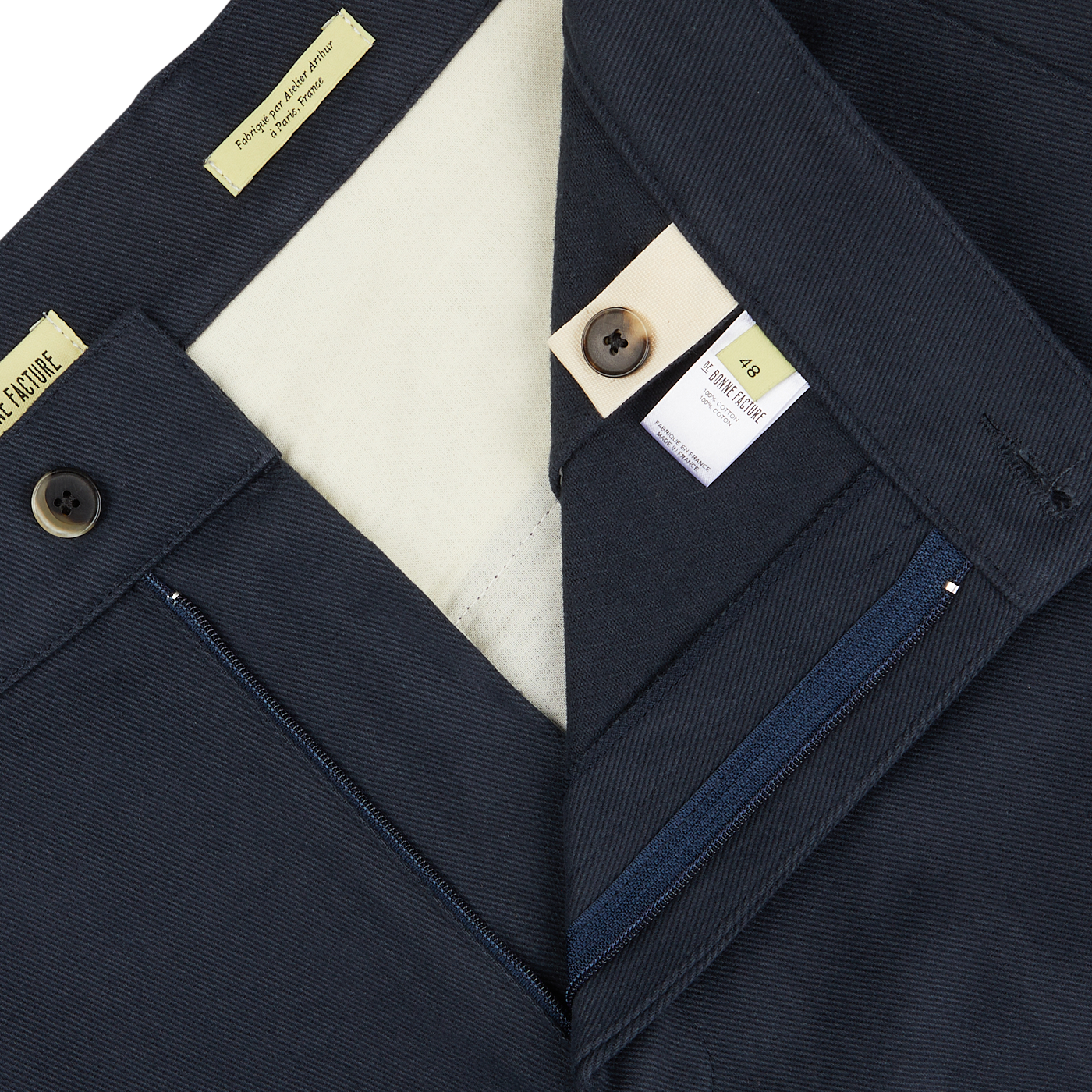 Close-up of De Bonne Facture navy blue men's coat made of heavy cotton drill fabric, with detailed labels and a button visible on the collar.