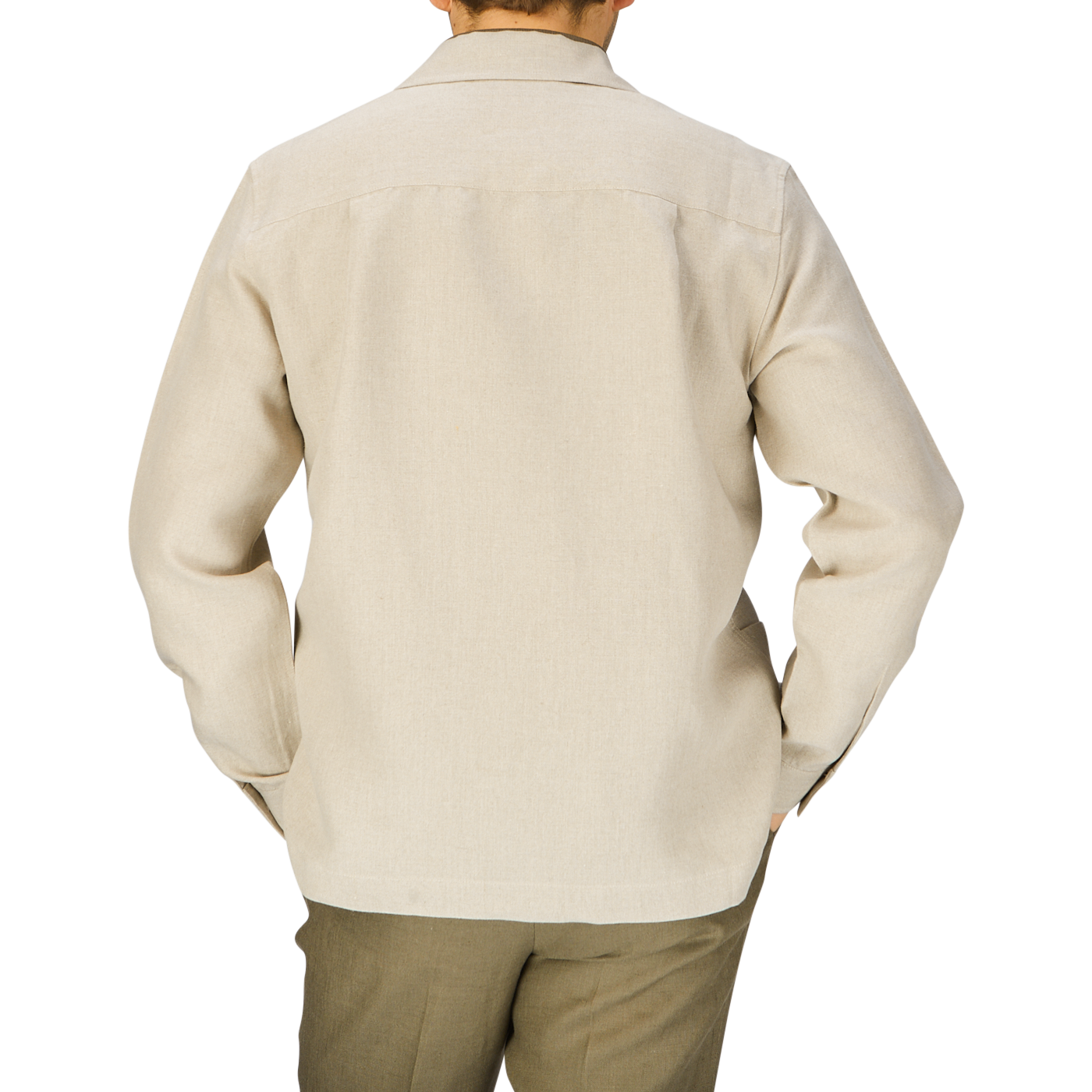 A man viewed from behind, wearing an unbuttoned Oatmeal Beige Linen Canvas Painter's Jacket by De Bonne Facture and dark green trousers, standing against a light gray background.