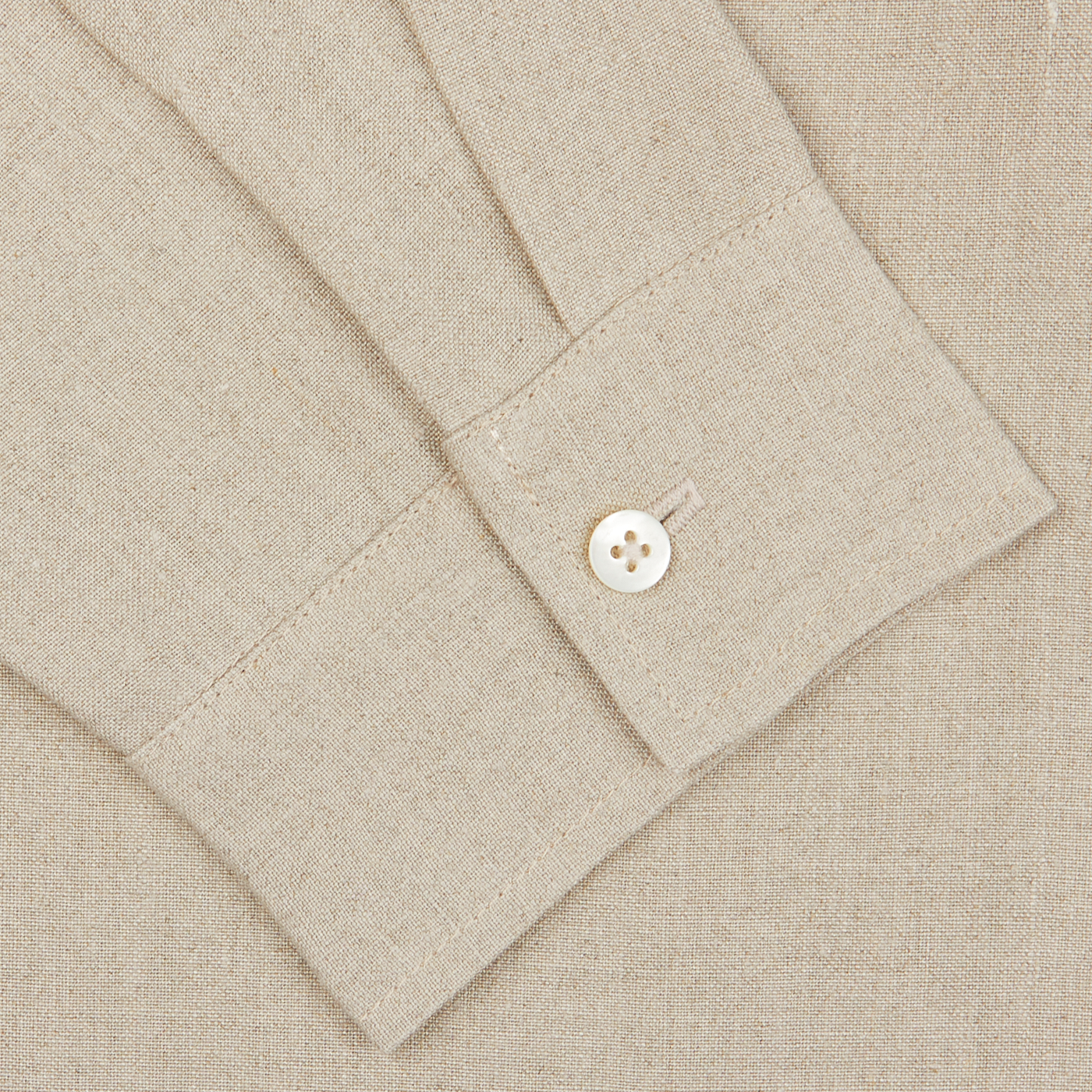 Close-up of a De Bonne Facture oatmeal beige linen canvas painter’s jacket with a detailed view of a cuff featuring a button, showcasing the texture and stitching.