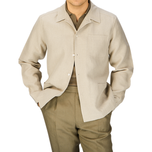A man dressed in a Oatmeal Beige Linen Canvas Painter's Jacket by De Bonne Facture and green trousers standing against a light background.