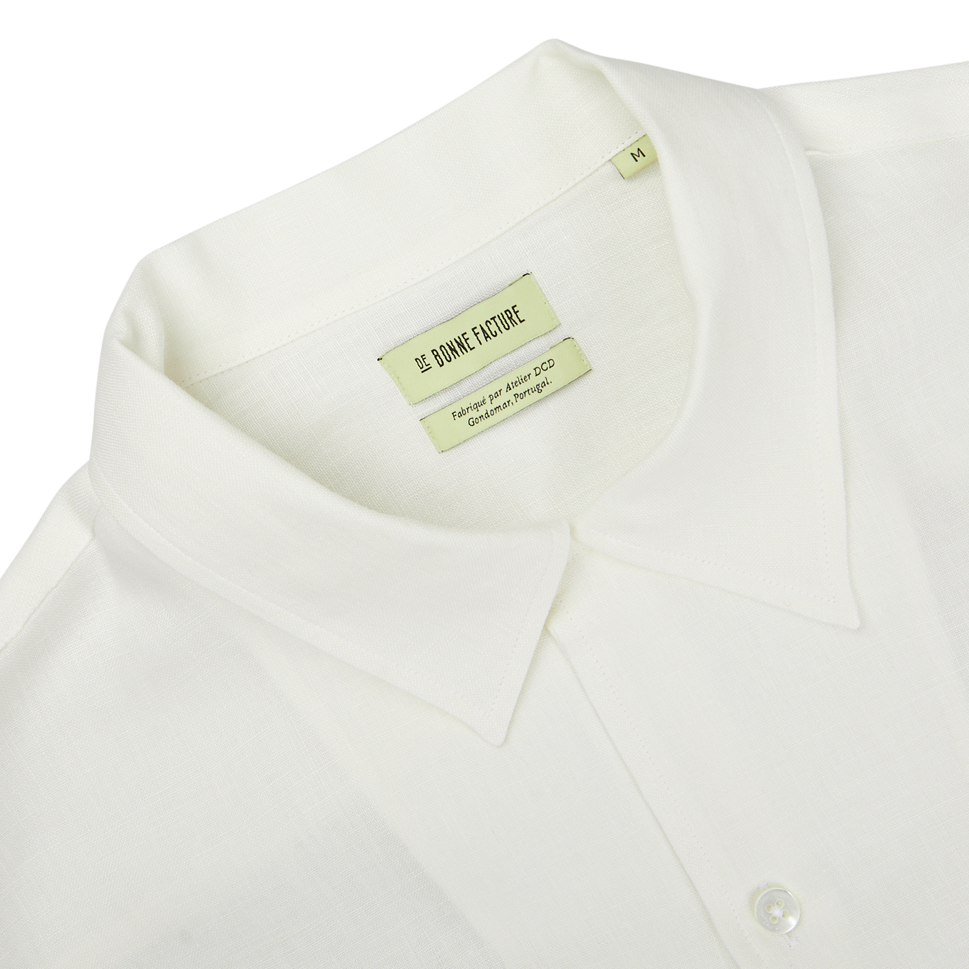Close-up of an Off White Linen Floral Embroidered Shirt with a Garden of Eden embroidery and a green label inside showing the brand name "De Bonne Facture" and size "M".