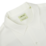 Close-up of an Off White Linen Floral Embroidered Shirt with a Garden of Eden embroidery and a green label inside showing the brand name "De Bonne Facture" and size "M".