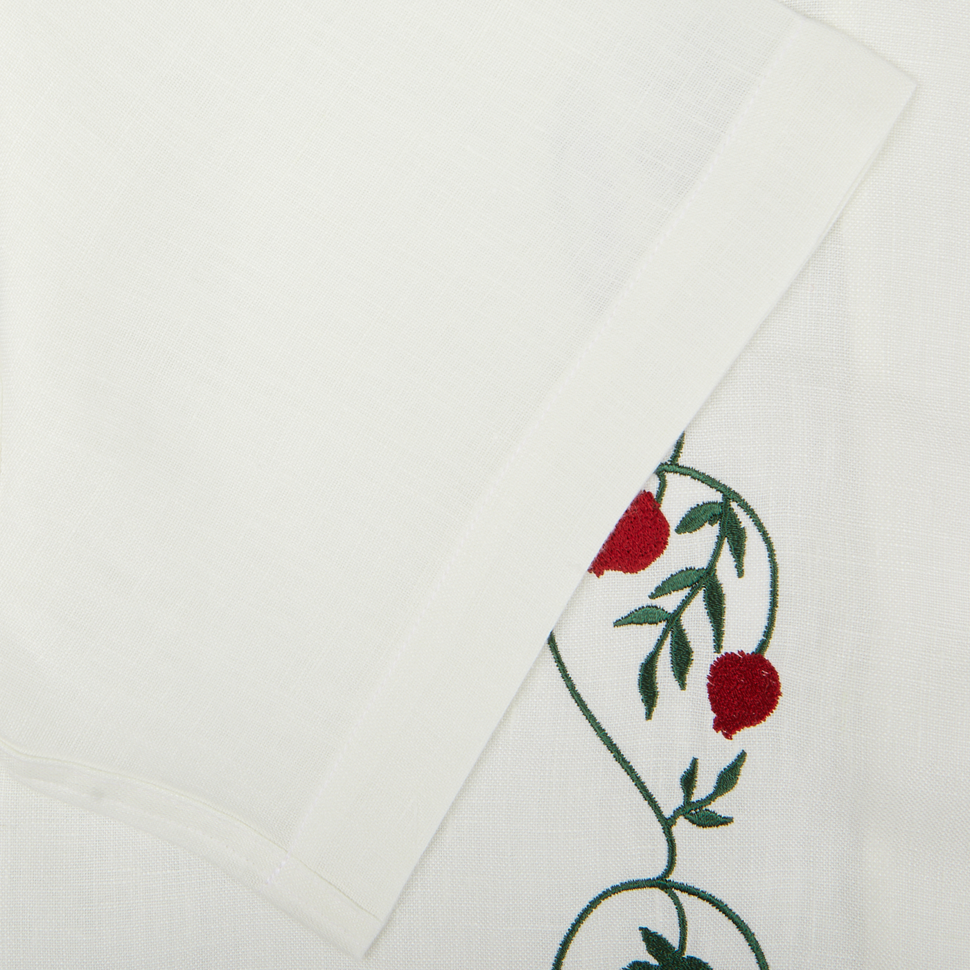 Off White Linen Floral Embroidered Shirt folded on a table, decorated with an embroidered design featuring red flowers and green leaves at one corner by De Bonne Facture.