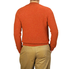 A person wearing a De Bonne Facture Orange Shetland Shaggy Dog Sweater and beige khaki pants, seen from behind. The background is plain and light-colored.