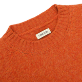 Close-up of an Orange Shetland Shaggy Dog Sweater with a ribbed neckline, featuring a tag that reads "De Bonne Facture." Made from pure Shetland wool, this regular-fit piece embodies warmth and style.