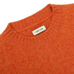 Close-up of an Orange Shetland Shaggy Dog Sweater with a ribbed neckline, featuring a tag that reads "De Bonne Facture." Made from pure Shetland wool, this regular-fit piece embodies warmth and style.